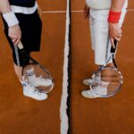 Two tennis players stand on a clay court with rackets, ready for a match.
